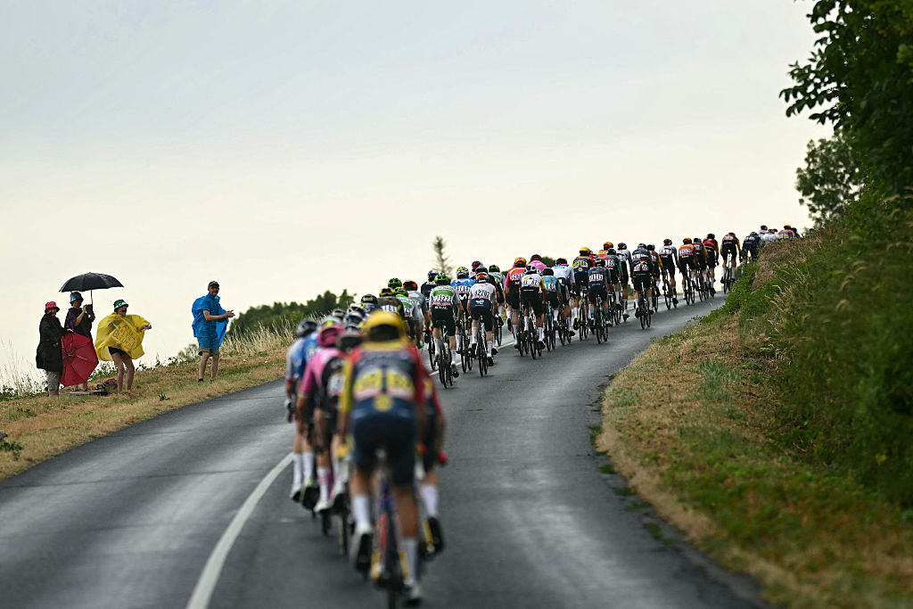 Spectators with umbrellas and rain capes cheer the pack of riders (peloton) as they cycle in the rain during the 11th stage of the 113th edition of the Tour de France cycling race, 161,3 km between Vichy and Nevers in central France, on July 15, 2026. (Photo by Loic VENANCE / AFP)