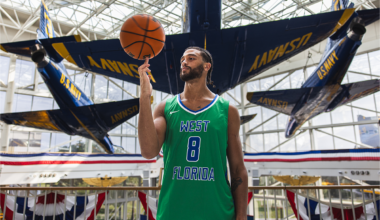 UWF men's basketball player with jersey number 8 spins a basketball on his finger while standing in front of a U.S. Navy Blue Angels aircraft.