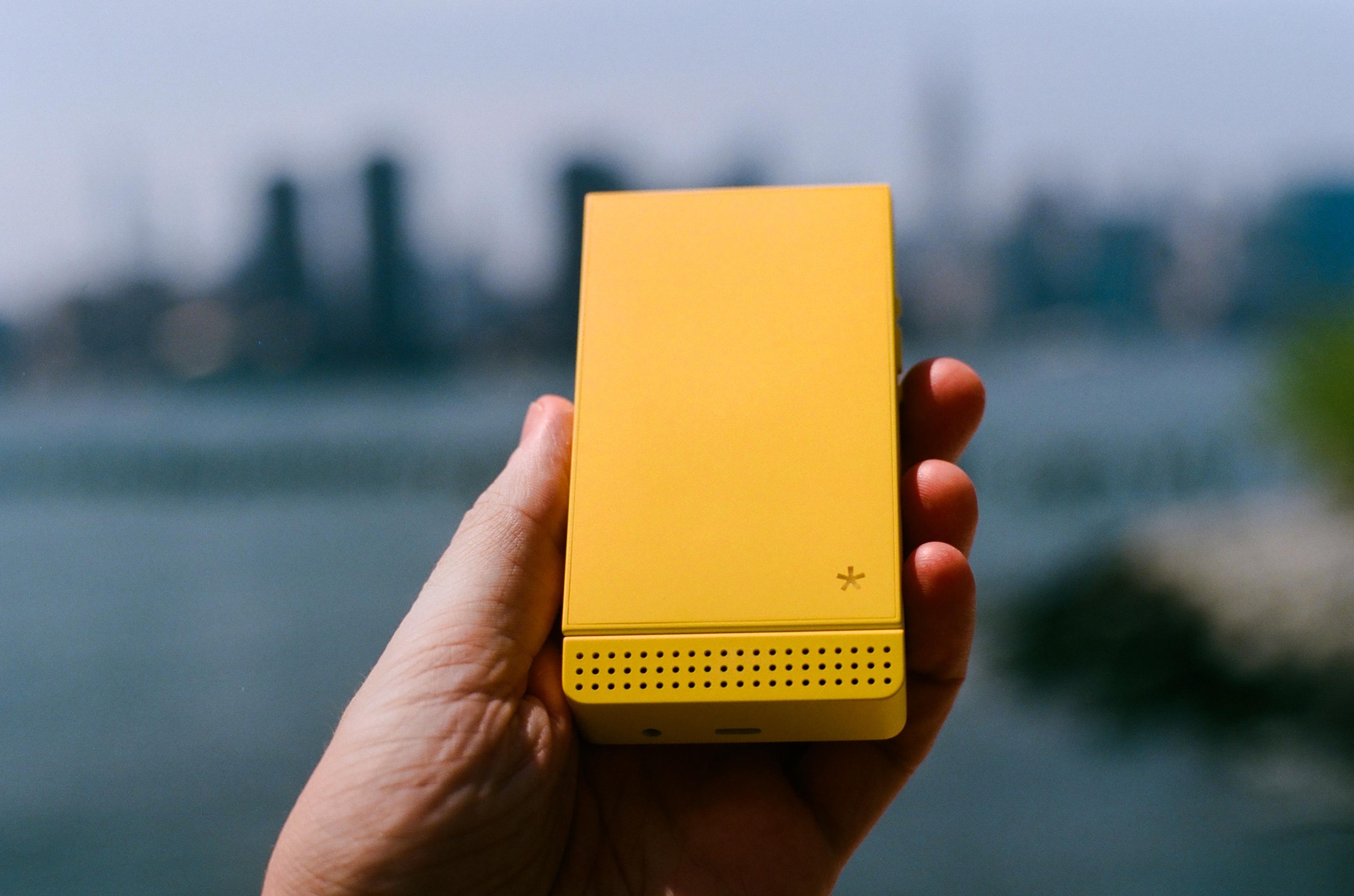 A yellow flip phone, closed, in front of a skyline.