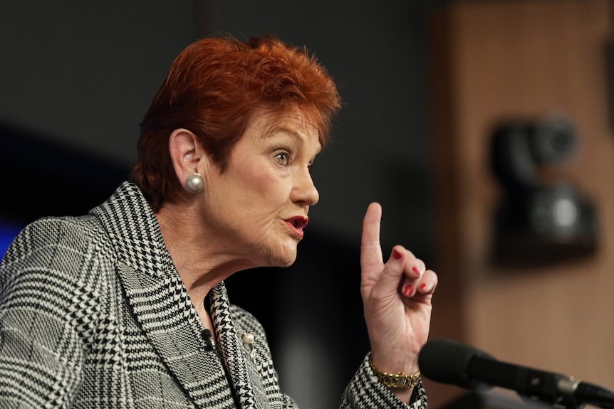 A woman with red hair speaks at a lectern.