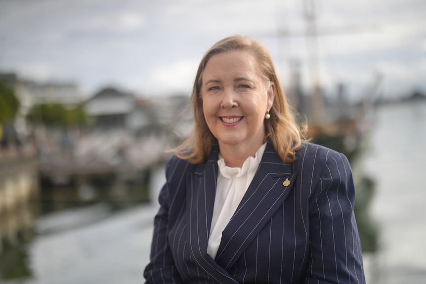 Woman with a white shirt and navy blazer sitting by a harbour.
