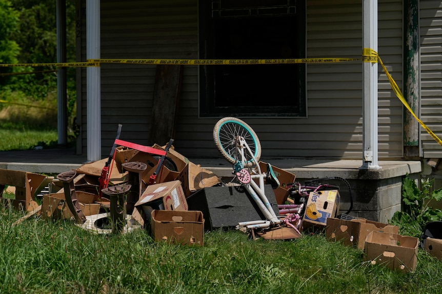 A pile of discarded cardboard boxes and up-ended children's bicycles in front of a home's porch.
