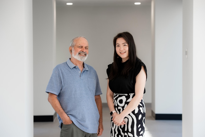 A man and a woman stand together and smile slightly at the camera.