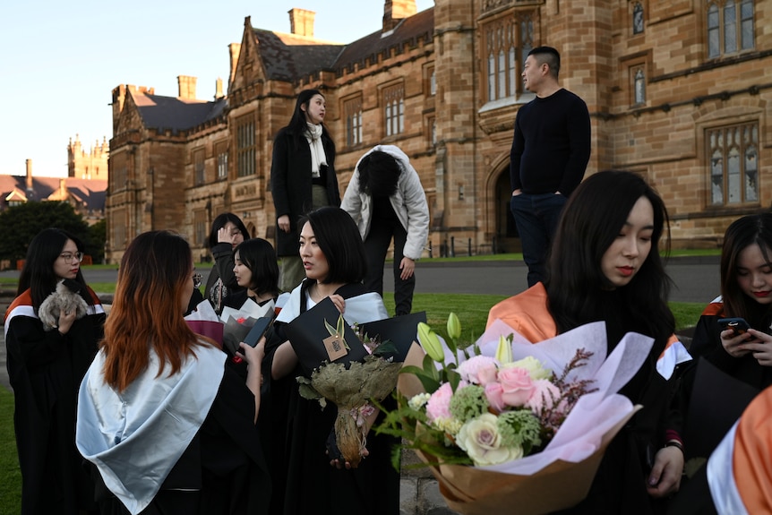 A group of students wearing graduation gowns and holding flowers.