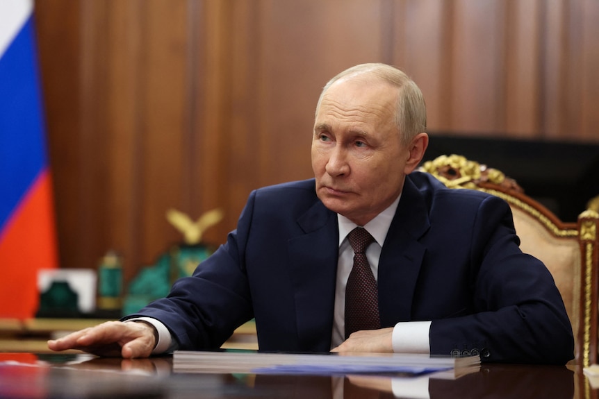 Russian President Vladimir Putin reaches his hand across a table