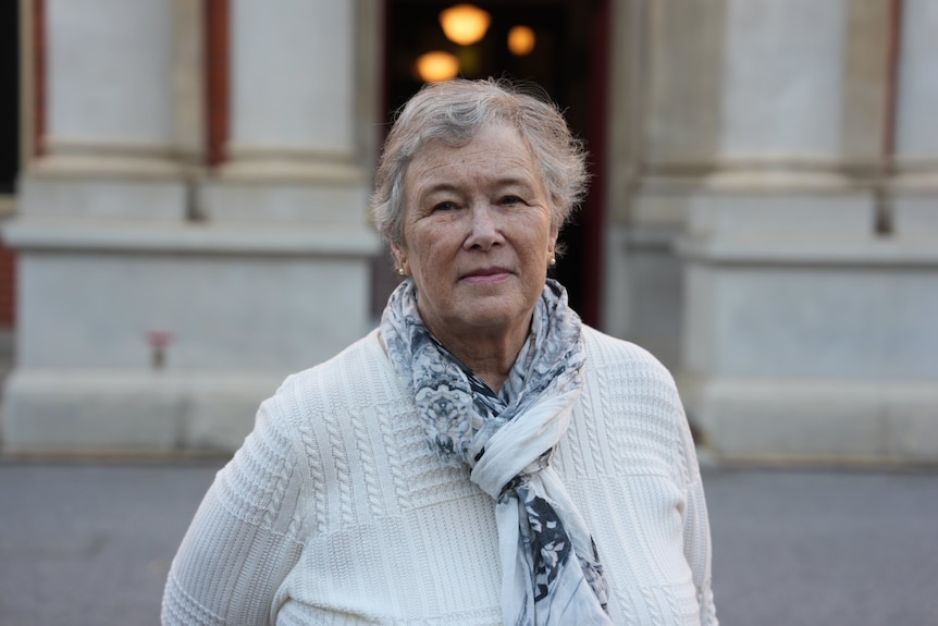 A mid-shot of a woman wearing a white knit and scarf 