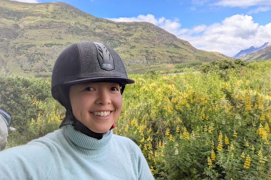 A woman wearing a helmet in front of a mountain and shrubs.