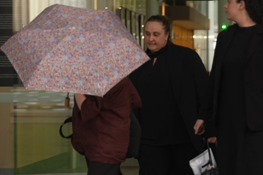 A person with an umbrella and two other women walking out of court.