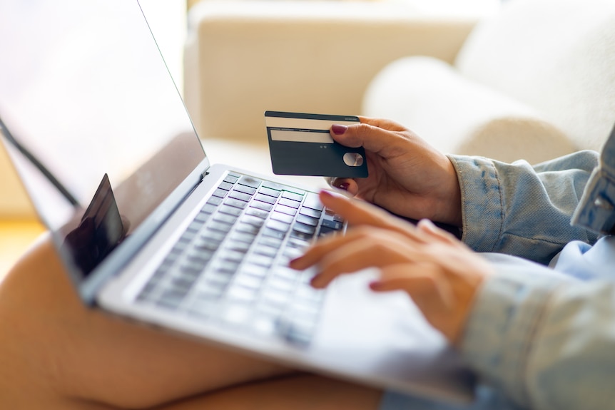 Woman with laptop holding her bank card while typing, close up of computer and hands only.