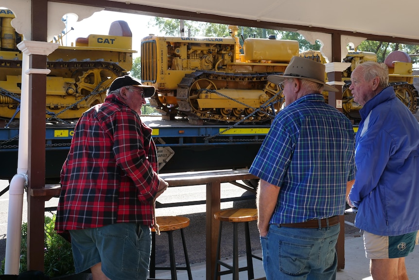 three people under a canopy chatting and looking at yellow tractor