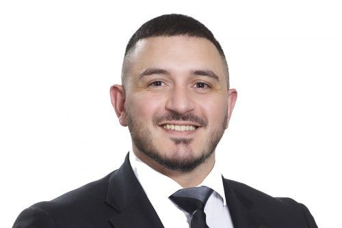 A man in a black and white suit smiles for a professional portrait.