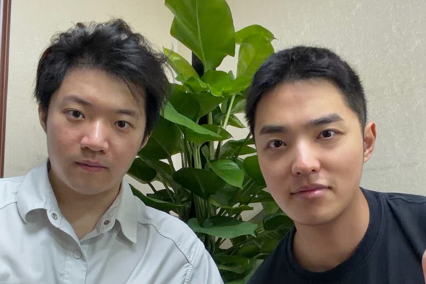 Two men sit next to each other, looking at the camera.