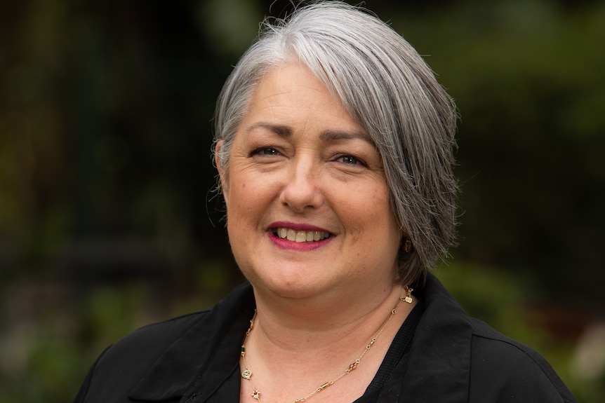 A woman with grey hair and a black shirt is smiling at the camera.