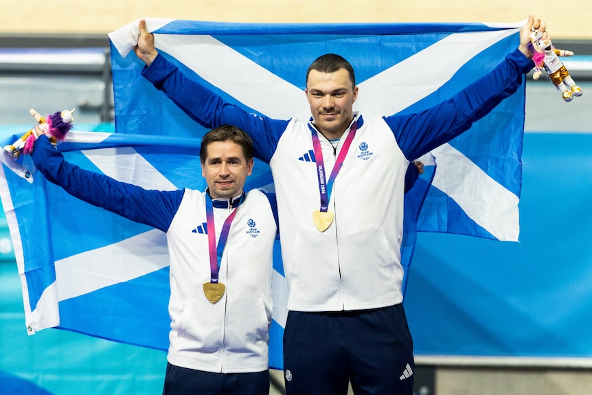 Neil Fache and Aaron Pope hold Scotland flags on the cycling podium.