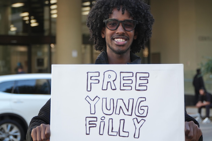 A young man holds a Free Yung Filly sign