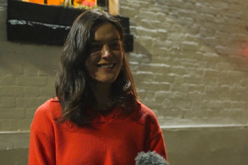 Woman standing in front of a white brick wall with a red sweater.