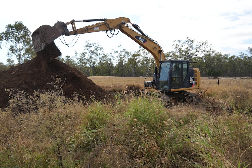 An excavator dumping dirt onto a levy bank