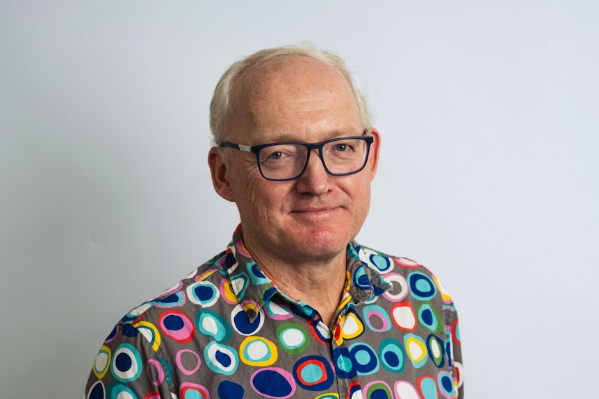 A portrait shot of a balding man with glasses and a colourful shirt.