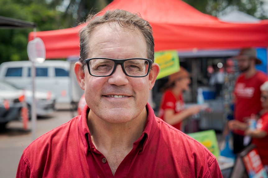 A man standing outside a tent at some outdoor markets and smiling.