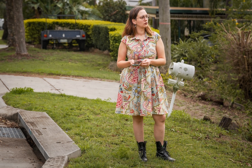 A woman in a floral dress holds her phone on the street looking at houses