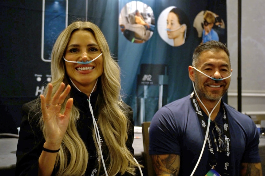 Ablonde woman and a brunette man smiling with tubes attached to their noses.