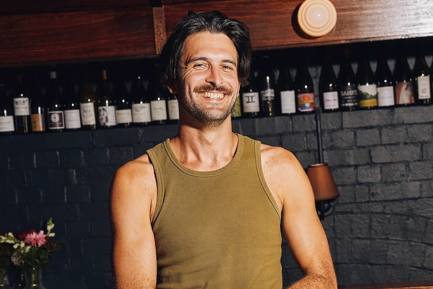 A man with brown hair smiling with his arms crossed wearing a green singlet.
