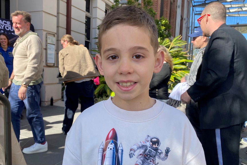 A young boy with brown hair looks at the camera smiling