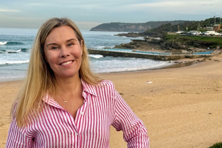 Woman with blonde hair standing in front of a beach.