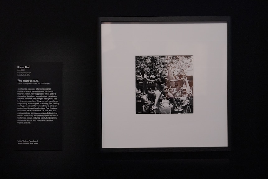 A photo of young Aboriginal girl on her dad's shoulders as they march with a group through the city, on display in a gallery.