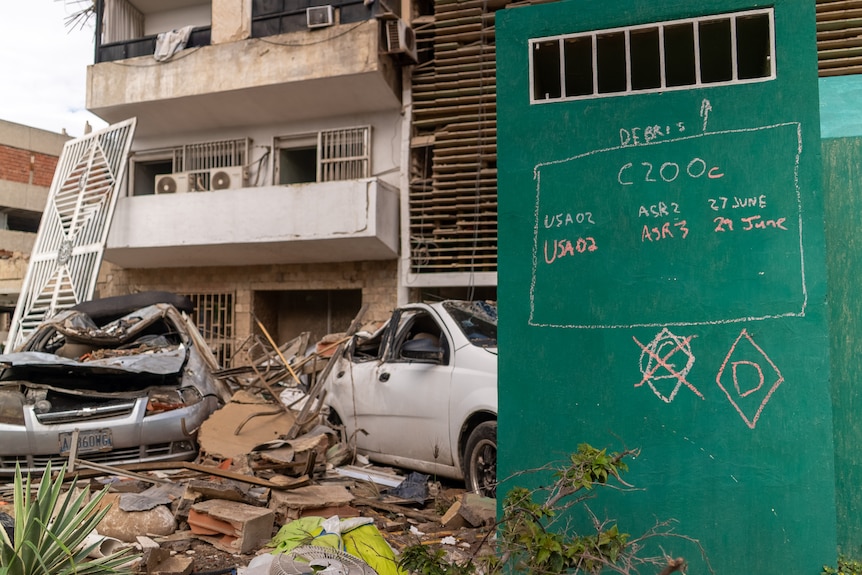 Wrecked cars and rubble in front of an apartment building.