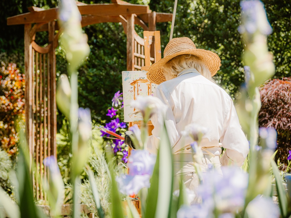 A woman paints on canvas in a sunny garden.