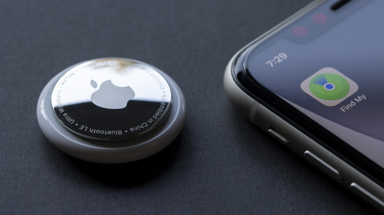 Apple AirTag beside an iPhone displaying the Find My app icon on the home screen.
