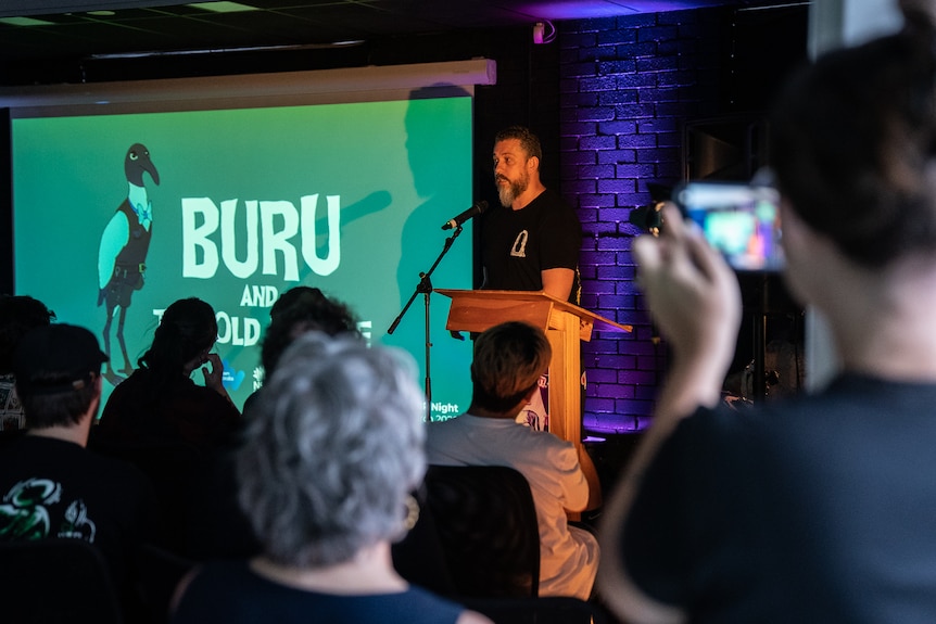 a man stands at a lecturn giving a speech with a picture of an ibis on a screen