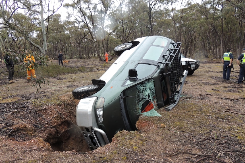 A car flipped on its side with its nose in a big hole in the ground.