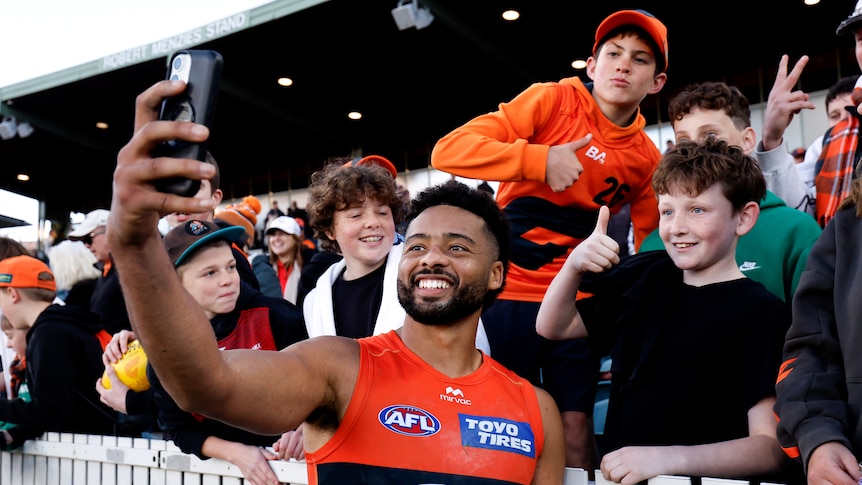A GWS AFL player smiles as he takes a selfie with a young fan after a win.