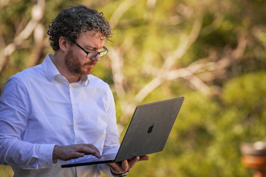 A man standing and holding a laptop in his hand.