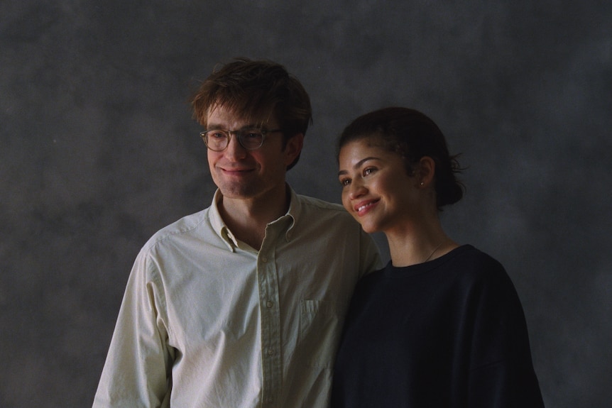 Robert Pattinson and Zendaya stand together in a photo studio with a grey marbled background