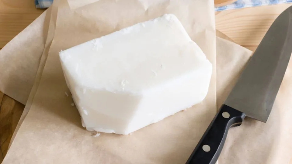 A rectangular block of white lard sits on brown parchment paper next to a large kitchen knife.