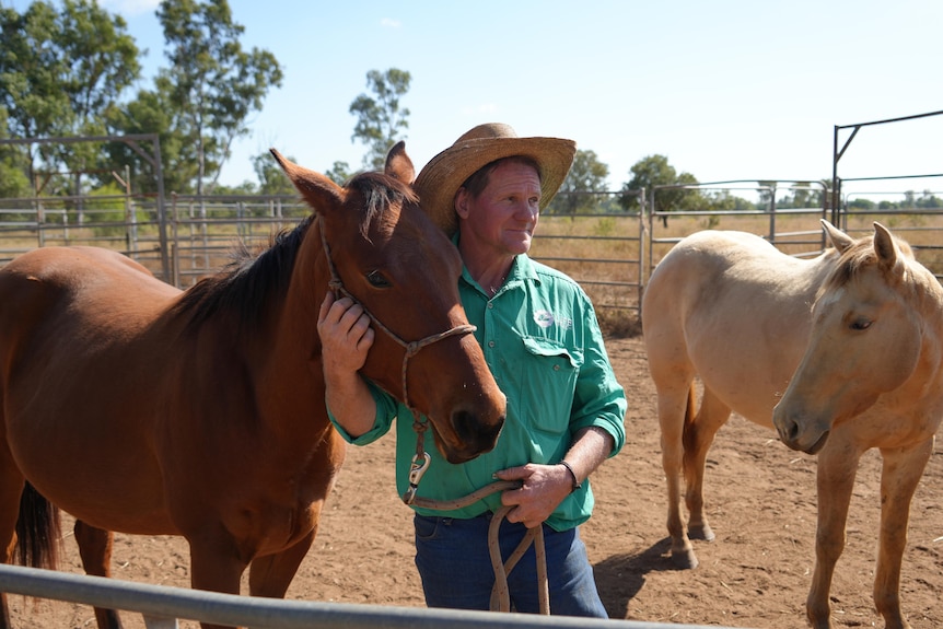 A man patting a horse by the neck, in a dusty yard.