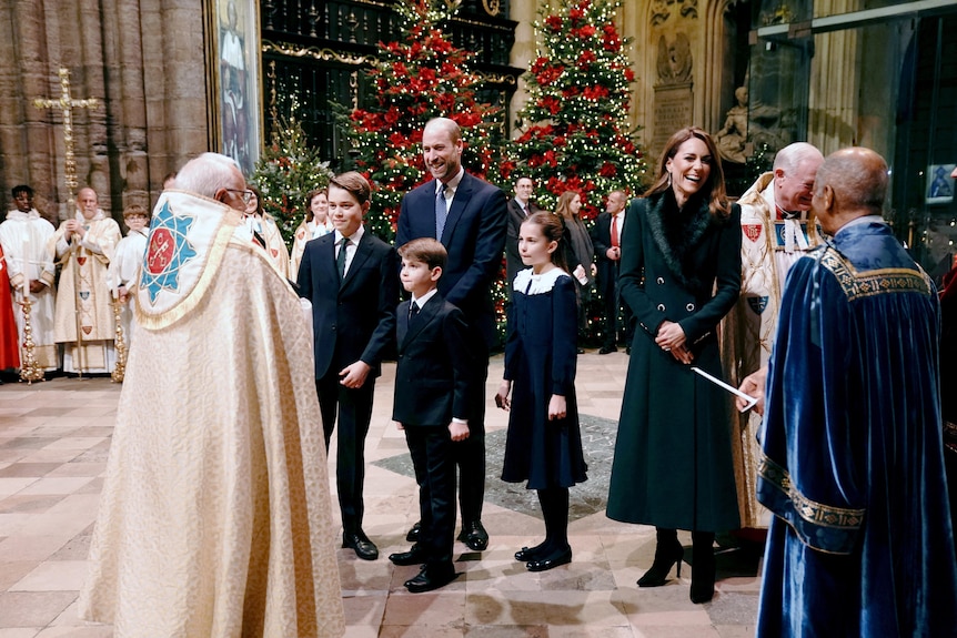 The royal family standing in front of a priest in a church.