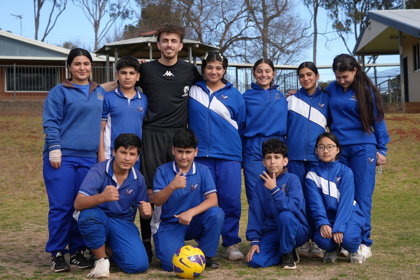 A man smiling with students and a soccer ball.