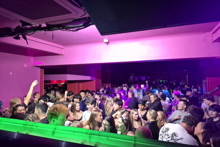 A nigh club filled with people dancing under the purple and green lights.