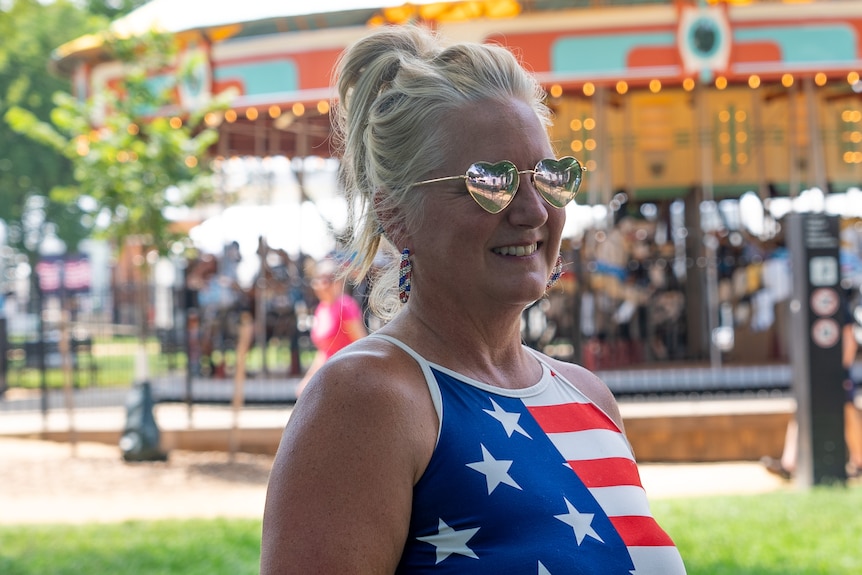Lisa Jox, pictured in front of a merry-go-round, wears a US flag shirt and heart-shaped sunglasses.