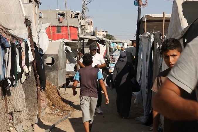 A child navigates a dirt path through tents in Gaza.