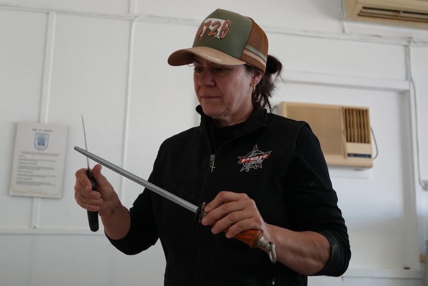 Female butcher sharpening knife on metal stick.