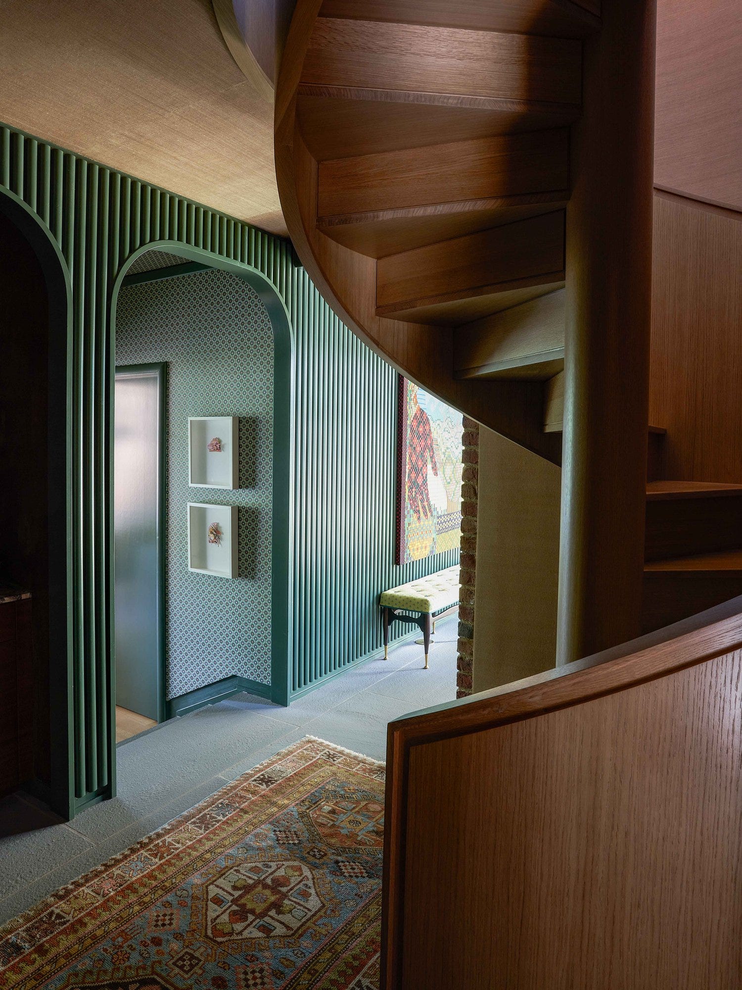 Spiral wooden staircase leading to a bright hallway with patterned walls and a decorative rug.