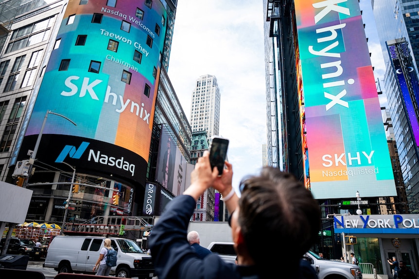 A man takes a photo using his smartphone of an electronic advertising board with the SK hynix logo.