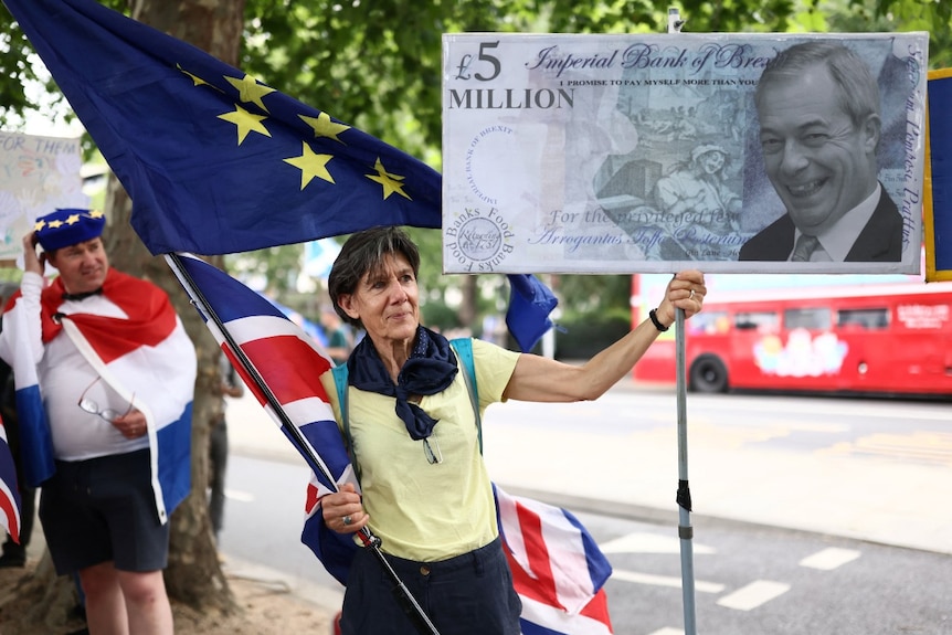 A woman holds a large sign with a picture of Nigel Farage on a £5 million bank note on it