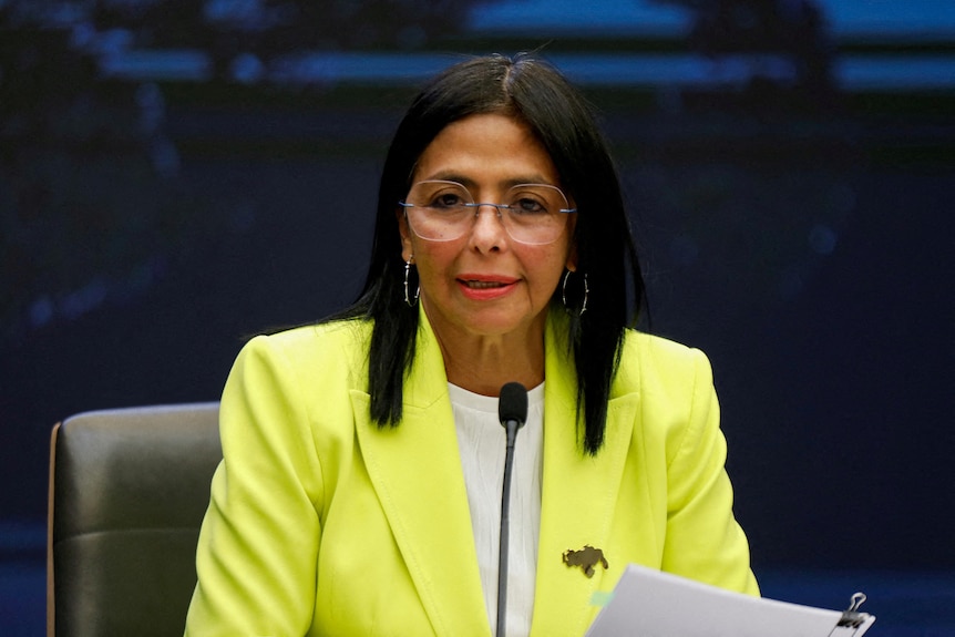 Delcy Rodriguez sits at a microphone and holds a piece of paper.
