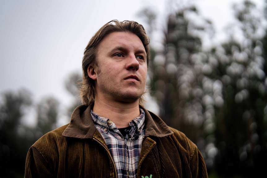 A young man looks out to the distance among trees.